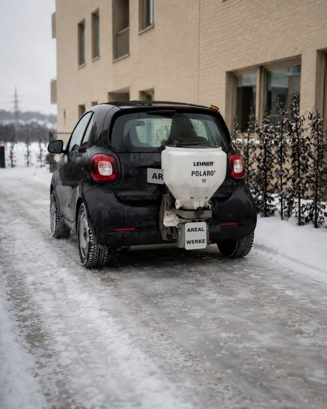 Winterdienst-Fahrzeug mit Streuautomat am Heck streut eine vereiste Zufahrt