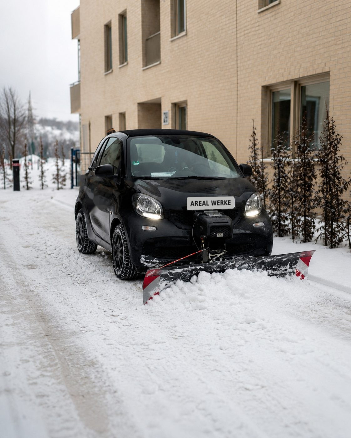 Kompaktes Räumfahrzeug mit Schneepflug räumt die verschneite Zufahrt einer Wohnüberbauung